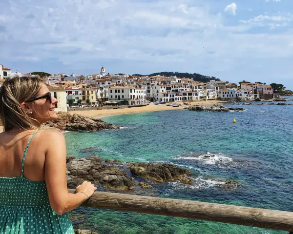 Mujer sonríe mirando el mar turquesa y las casas blancas de Calella de Palafrugell.
