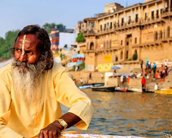 Un hombre con barba y marca en la frente navega en el Ganges, una escena típica al viajar a la India.