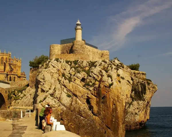 Descubre qué ver en Castro Urdiales: un faro en un castillo sobre rocas, con una iglesia gótica al fondo y gente paseando.