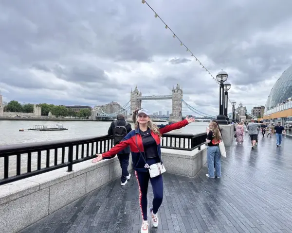 Mujer sonriente con brazos extendidos en Londres, con la Torre de Londres y el Tower Bridge al fondo. ¡Excelentes consejos para viajar a Londres!
