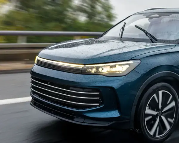 Un elegante coche seminuevo de color azul oscuro circula por una carretera mojada, con las luces encendidas.