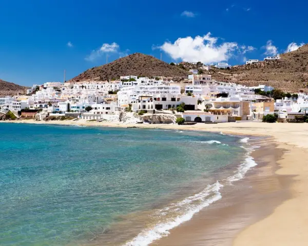Pueblo blanco a orillas del mar turquesa, ideal para descubrir qué ver en Cabo de Gata. Playas doradas y casas encaladas bajo un cielo azul.