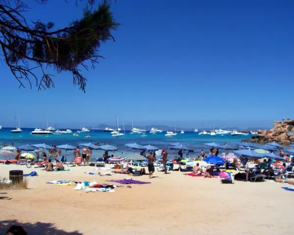 Playa con gente, sombrillas y barcos en el mar azul. Un día perfecto para ver qué ver en Formentera.