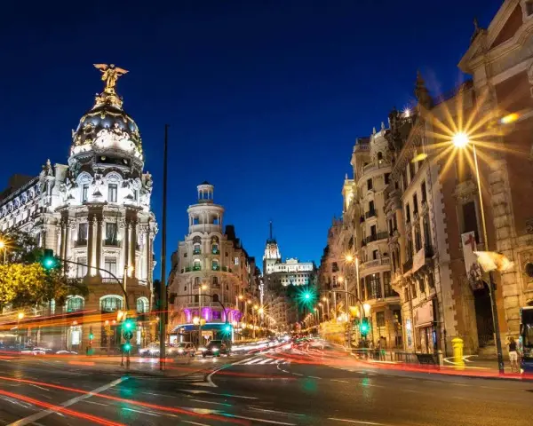 Noche vibrante en Madrid, con edificios iluminados y estelas de luz de coches. ¡Un fin de semana en Madrid inolvidable!