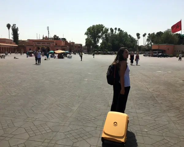Una mujer con mochila y maleta amarilla en una plaza de Marruecos. Piensa en qué llevar a Marruecos para este viaje.