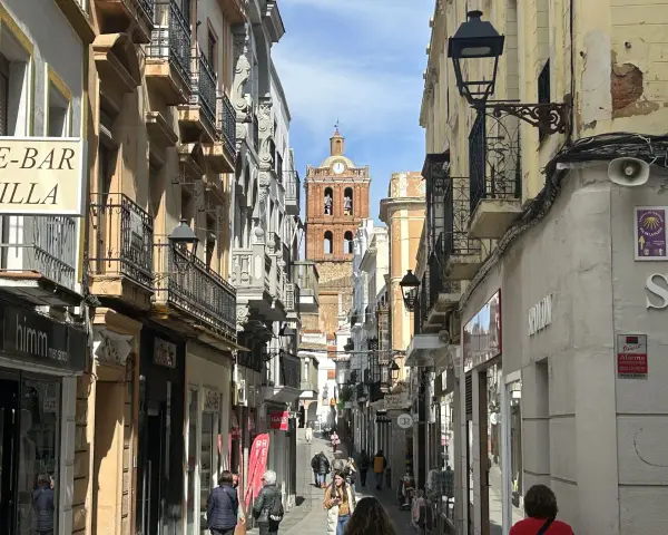 Calle comercial con edificios antiguos y un campanario al fondo. Descubre qué ver en Zafra y disfruta de su encanto.