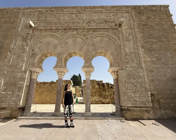 Mujer posa ante arcos de Medina Azahara. Se puede visitar Medina Azahara por libre, explorando su rica historia y arquitectura.