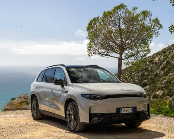Un SUV blanco moderno, uno de los tipos de coches eléctricos, aparcado en un camino de tierra con el mar y una colina verde de fondo.