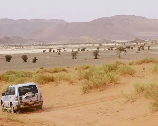 Un todoterreno blanco avanza por dunas de arena en un paisaje desértico de Marruecos. ¡Una aventura de Marruecos 5 días!