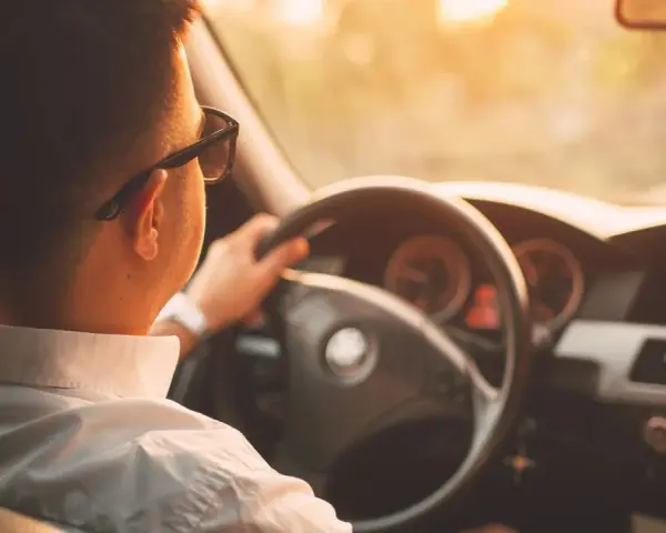 Hombre con gafas de sol conduce al atardecer. ¡Cuidado con la velocidad, te pueden multar!