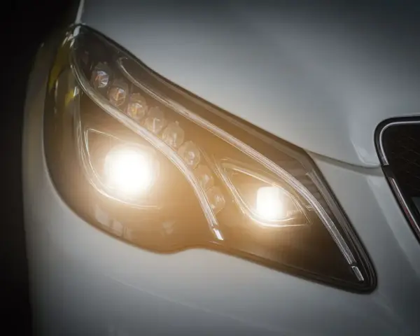 Primer plano de un faro de coche moderno con luces cortas encendidas, un símbolo de visibilidad y seguridad en la carretera.