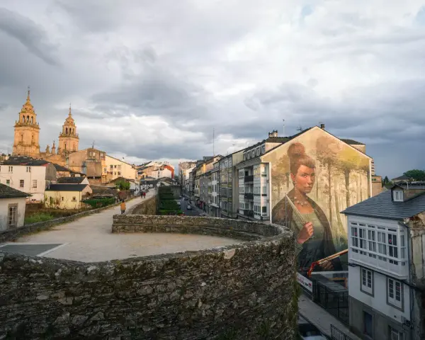 Mural de mujer en edificio, con la muralla romana y la catedral al fondo. Imprescindible que ver en Lugo.