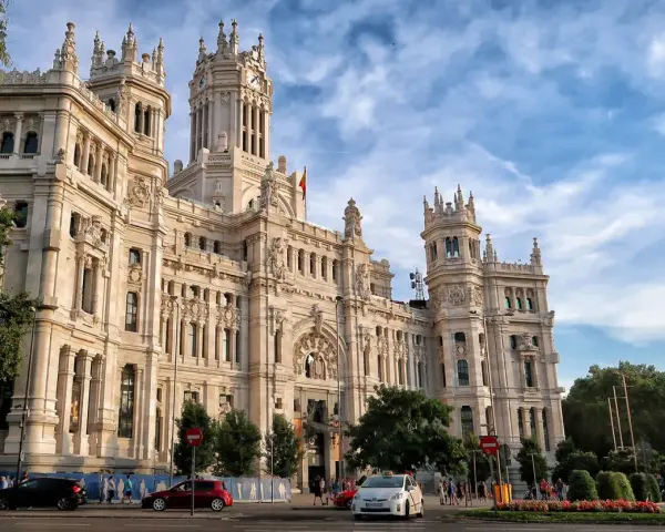 Un día en Madrid: el Palacio de Cibeles, un taxi blanco y coches circulan bajo un cielo azul con nubes.