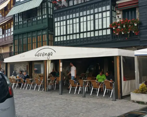 Gente disfrutando de una comida en Lekeitio, sentados en mesas al aire libre bajo un toldo blanco.