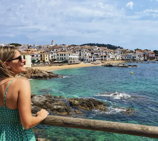 Mujer sonríe mirando el mar turquesa y las casas blancas de Calella de Palafrugell.