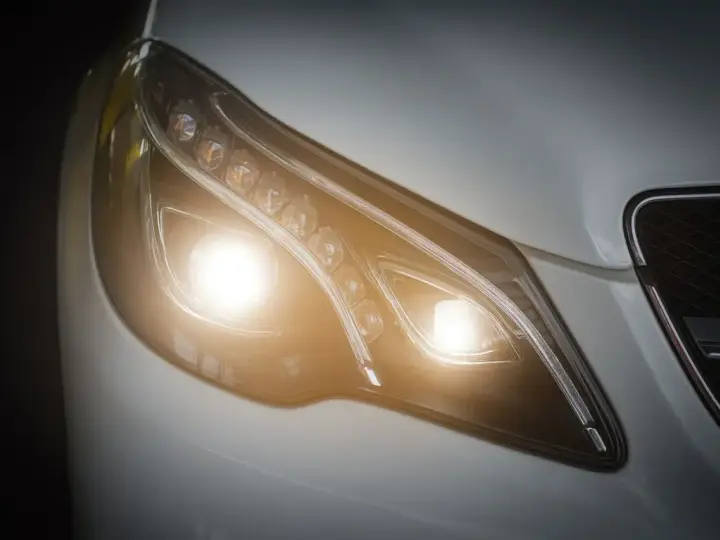 Primer plano de un faro de coche moderno con luces cortas encendidas, un símbolo de visibilidad y seguridad en la carretera.