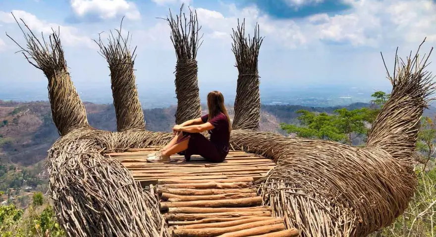 Mujer sentada en una mano gigante de ramas, disfrutando de la vista. Un lugar perfecto para viajar a Java, Indonesia.