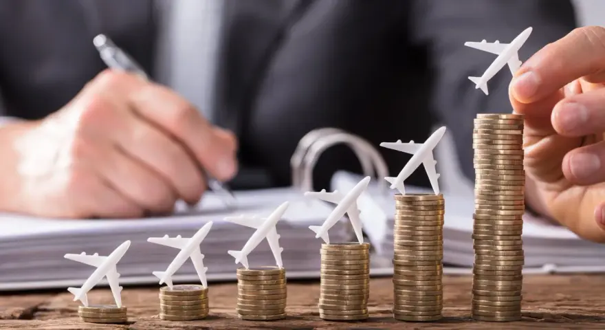 Pequeños aviones sobre pilas de monedas crecientes, simbolizando cómo viajar barato es posible con planificación.