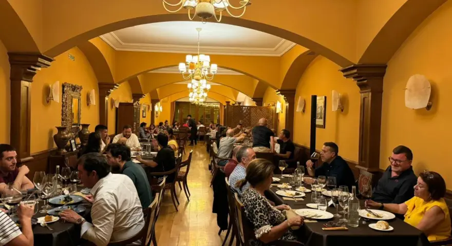 Gente disfrutando de una cena en un elegante restaurante con arcos y lámparas doradas. Una experiencia culinaria memorable para comer en Olite.