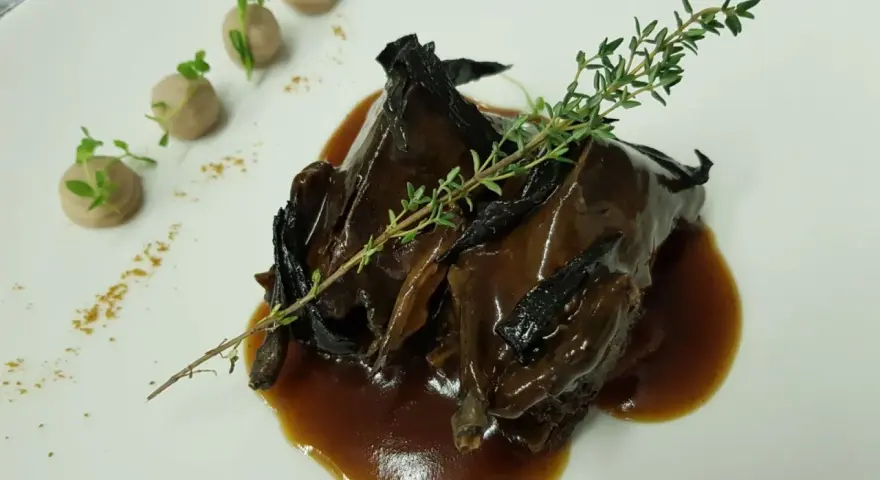 Plato de caza en salsa oscura, decorado con tomillo y puré de patatas. ¡Una opción deliciosa donde comer en Úbeda!