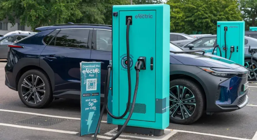 Coches eléctricos cargando. Las ventajas y desventajas de los coches eléctricos se reflejan en esta escena de carga, con un cartel que invita a descargar una app para ahorrar.