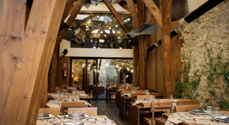 Mesas puestas en un restaurante rústico con vigas de madera y paredes de piedra, ideal para comer en Avilés.