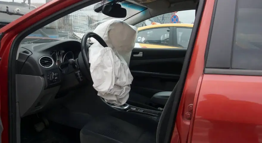 Interior de coche rojo con airbag del conductor desplegado, indicando la dirección del vehículo activa o pasiva tras un impacto.
