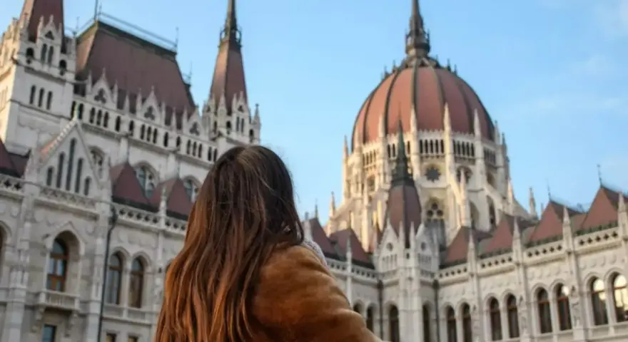 Mujer con abrigo de pelo admira el Parlamento de Budapest, un destino ideal donde viajar en noviembre en Europa.