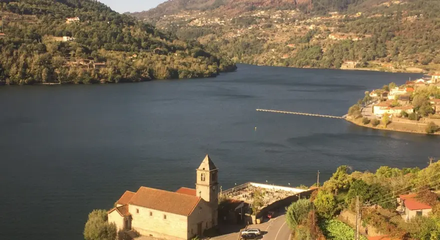 Un pueblo pintoresco a orillas de un río, con una iglesia y un cementerio. Las colinas verdes y las casas se extienden hasta donde alcanza la vista. ¡Un lugar ideal para ir a toro!