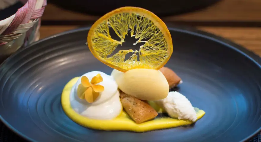 Postre de autor con helado de limón, merengue, bizcocho y naranja deshidratada. ¡Una delicia para saber dónde comer en Barcelona!