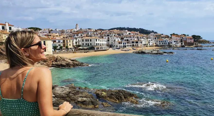 Mujer sonríe mirando el mar turquesa y las casas blancas de Calella de Palafrugell.