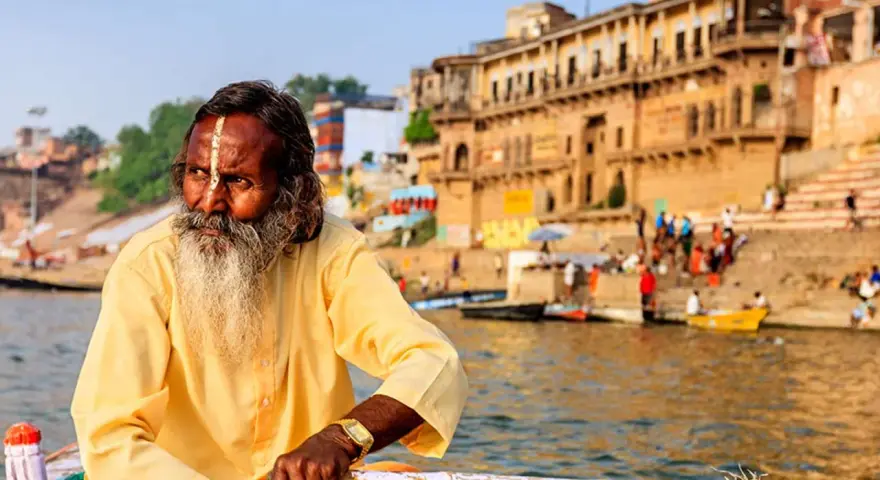 Un hombre con barba y marca en la frente navega en el Ganges, una escena típica al viajar a la India.