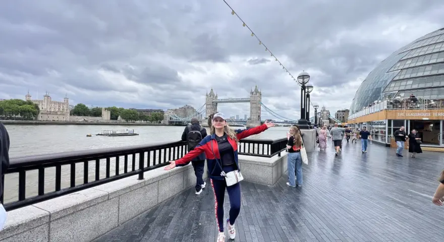 Mujer sonriente con brazos extendidos en Londres, con la Torre de Londres y el Tower Bridge al fondo. ¡Excelentes consejos para viajar a Londres!