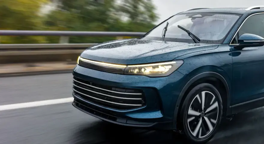 Un elegante coche seminuevo de color azul oscuro circula por una carretera mojada, con las luces encendidas.