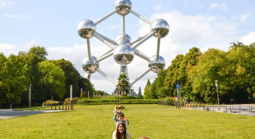 Familia posa frente al Atomium, un icono de que ver en Bruselas. Un niño salta detrás de su madre en el césped.