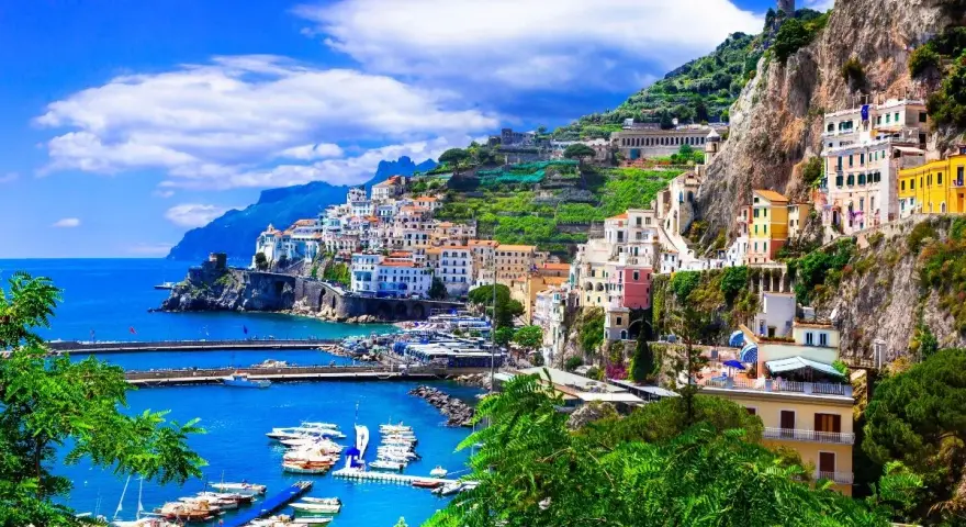 Un pueblo costero italiano con casas coloridas en laderas verdes, un puerto con barcos y el mar azul. ¡Un destino perfecto donde viajar en junio!