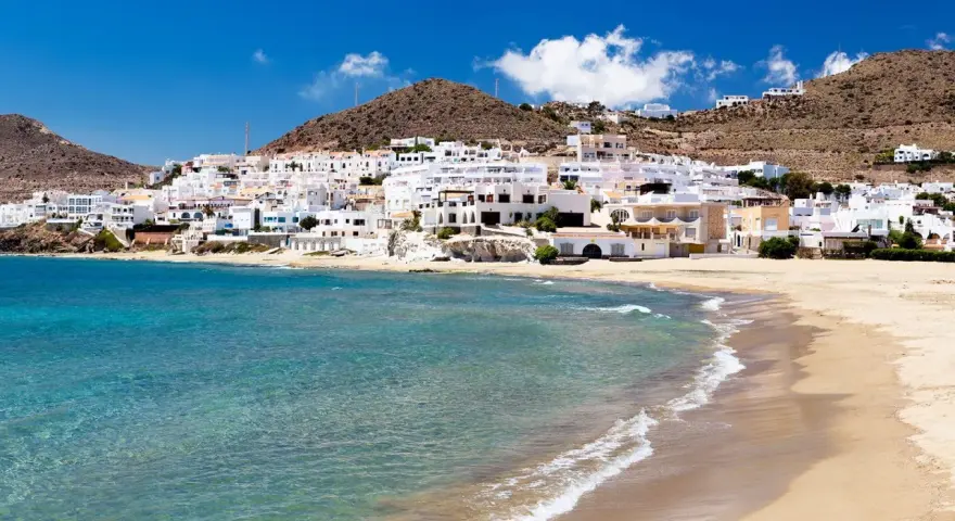 Pueblo blanco a orillas del mar turquesa, ideal para descubrir qué ver en Cabo de Gata. Playas doradas y casas encaladas bajo un cielo azul.