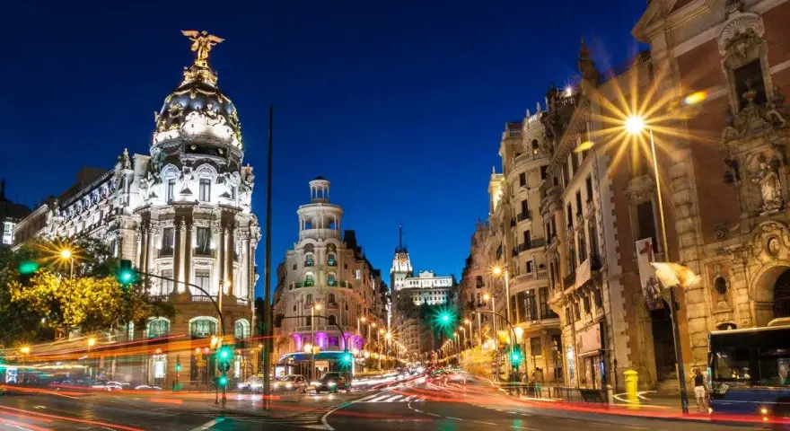 Noche vibrante en Madrid, con edificios iluminados y estelas de luz de coches. ¡Un fin de semana en Madrid inolvidable!