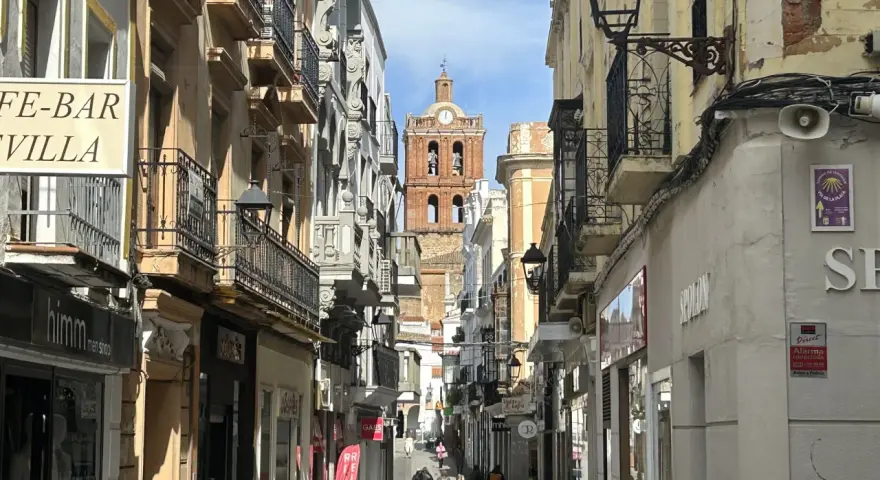 Calle comercial con edificios antiguos y un campanario al fondo. Descubre qué ver en Zafra y disfruta de su encanto.