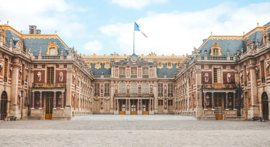 Palacio de Versalles, una visita obligada si buscas qué ver en París en 2 días. Majestuosa arquitectura y bandera francesa ondeando.