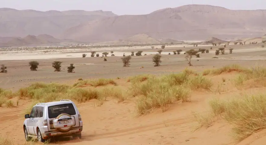 Un todoterreno blanco avanza por dunas de arena en un paisaje desértico de Marruecos. ¡Una aventura de Marruecos 5 días!