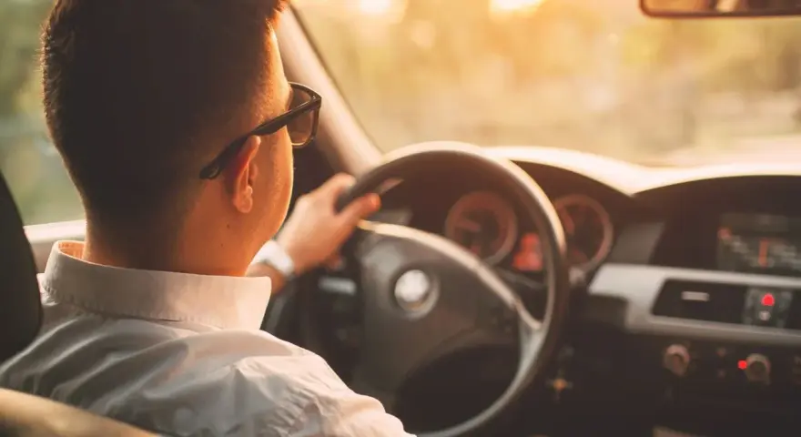 Hombre con gafas de sol conduce al atardecer. ¡Cuidado con la velocidad, te pueden multar!
