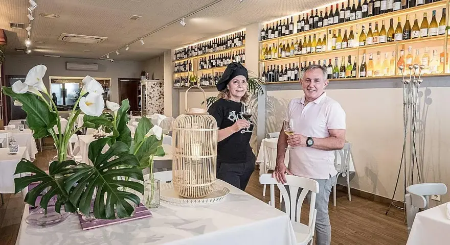 Pareja sonriente en un restaurante con estanterías llenas de vino. Un lugar ideal para saber donde comer en Logroño.