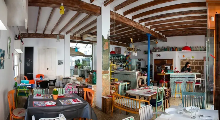 Un restaurante acogedor en Dénia, con mesas coloridas y vigas de madera. Ideal para saber donde comer en Dénia.