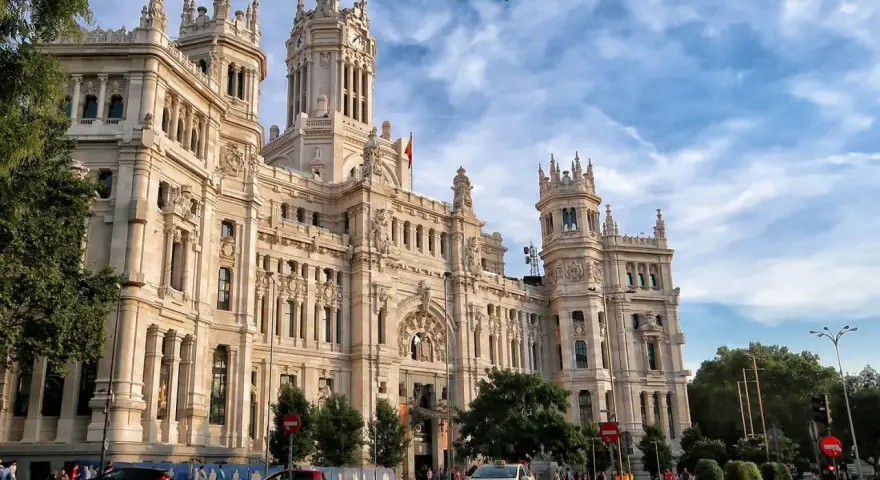 Un día en Madrid: el Palacio de Cibeles, un taxi blanco y coches circulan bajo un cielo azul con nubes.