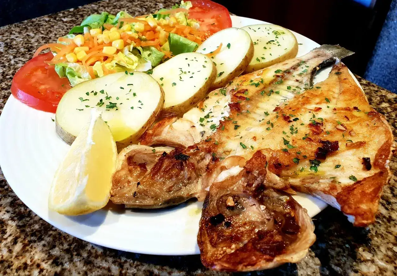 Un delicioso plato de pescado a la plancha con patatas, ensalada y lim&oacute;n. Una experiencia culinaria perfecta para comer en Mux&iacute;a.