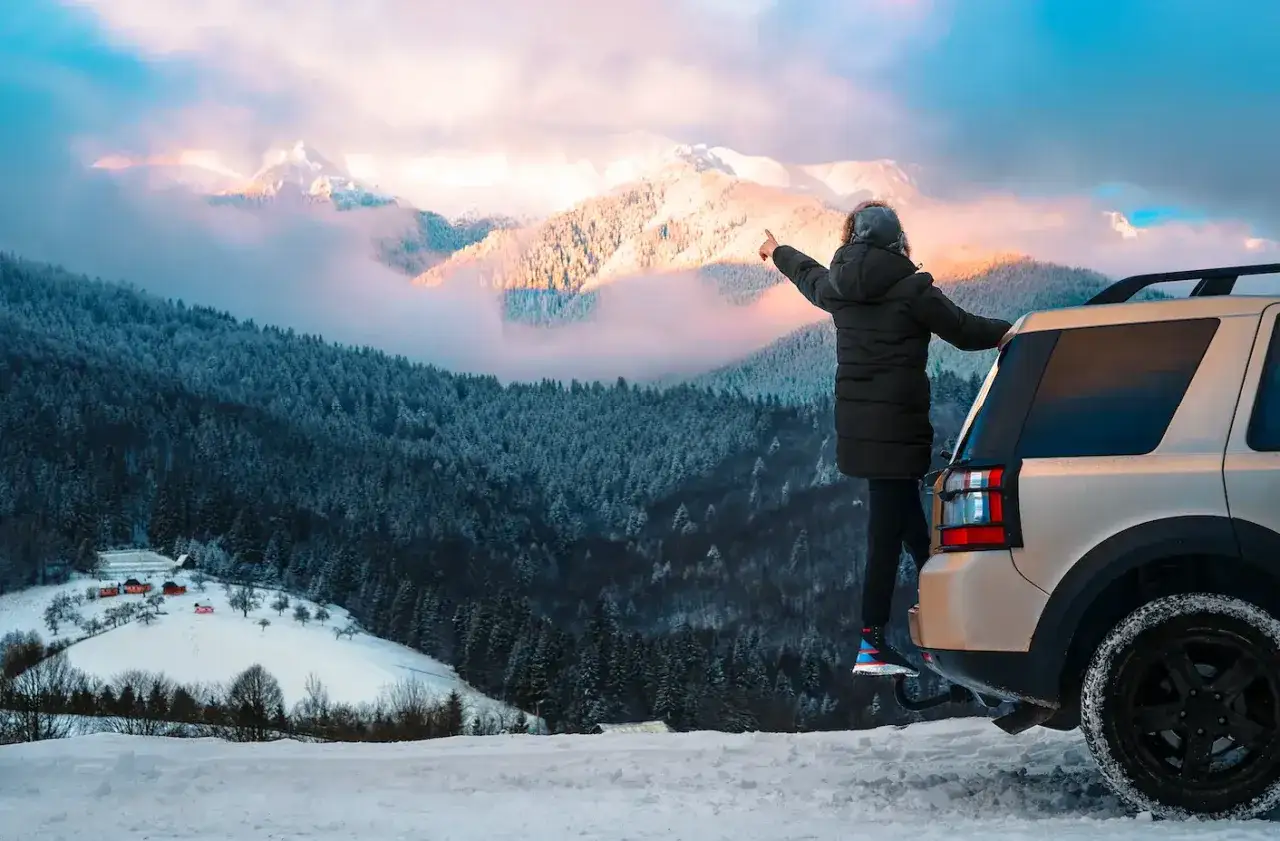 Persona se&ntilde;ala monta&ntilde;as nevadas desde un coche. &iexcl;Un destino ideal donde viajar en enero para disfrutar de paisajes espectaculares!