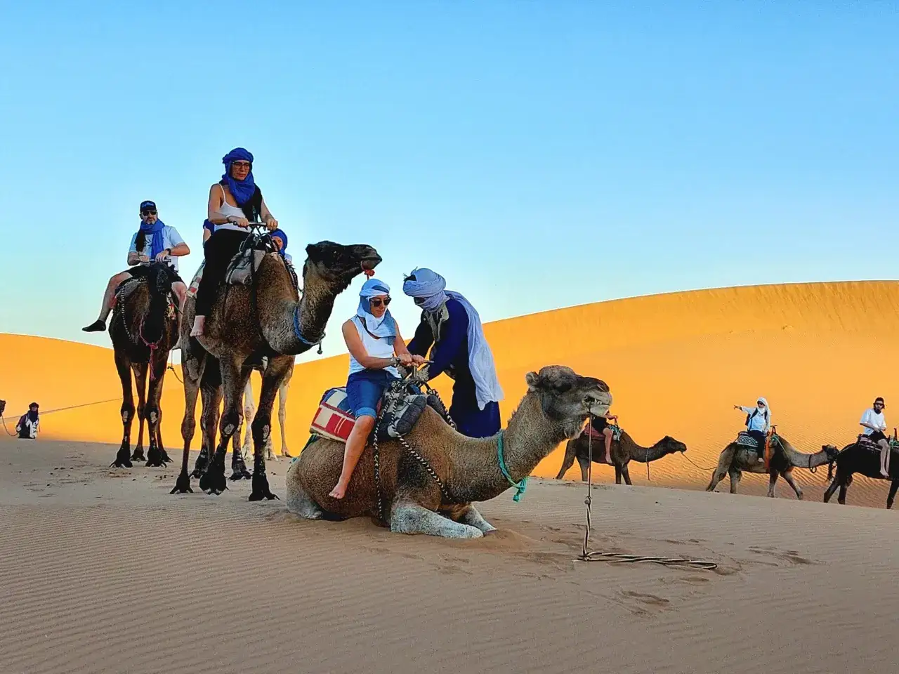 Viaje de marruecos 5 d&iacute;as: personas montan camellos en el desierto al atardecer.
