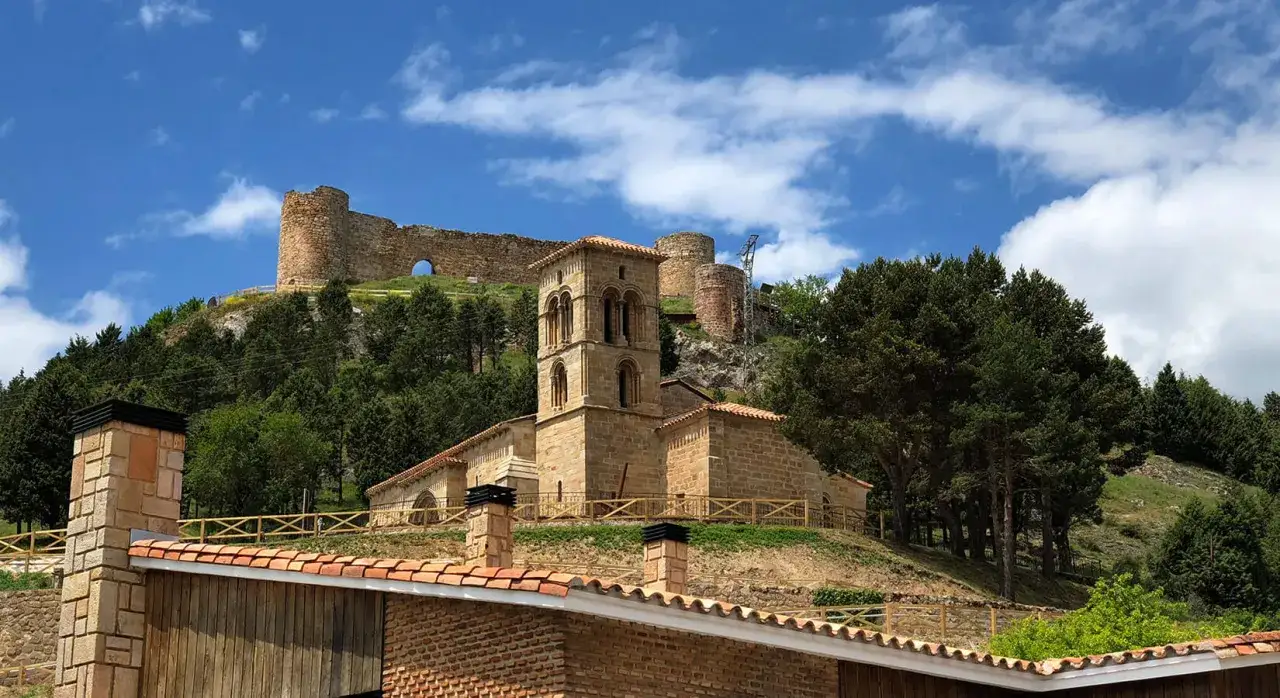 Iglesia rom&aacute;nica y castillo en ruinas en una colina verde. Un lugar hist&oacute;rico que ver en Palencia, con cielos azules y nubes.