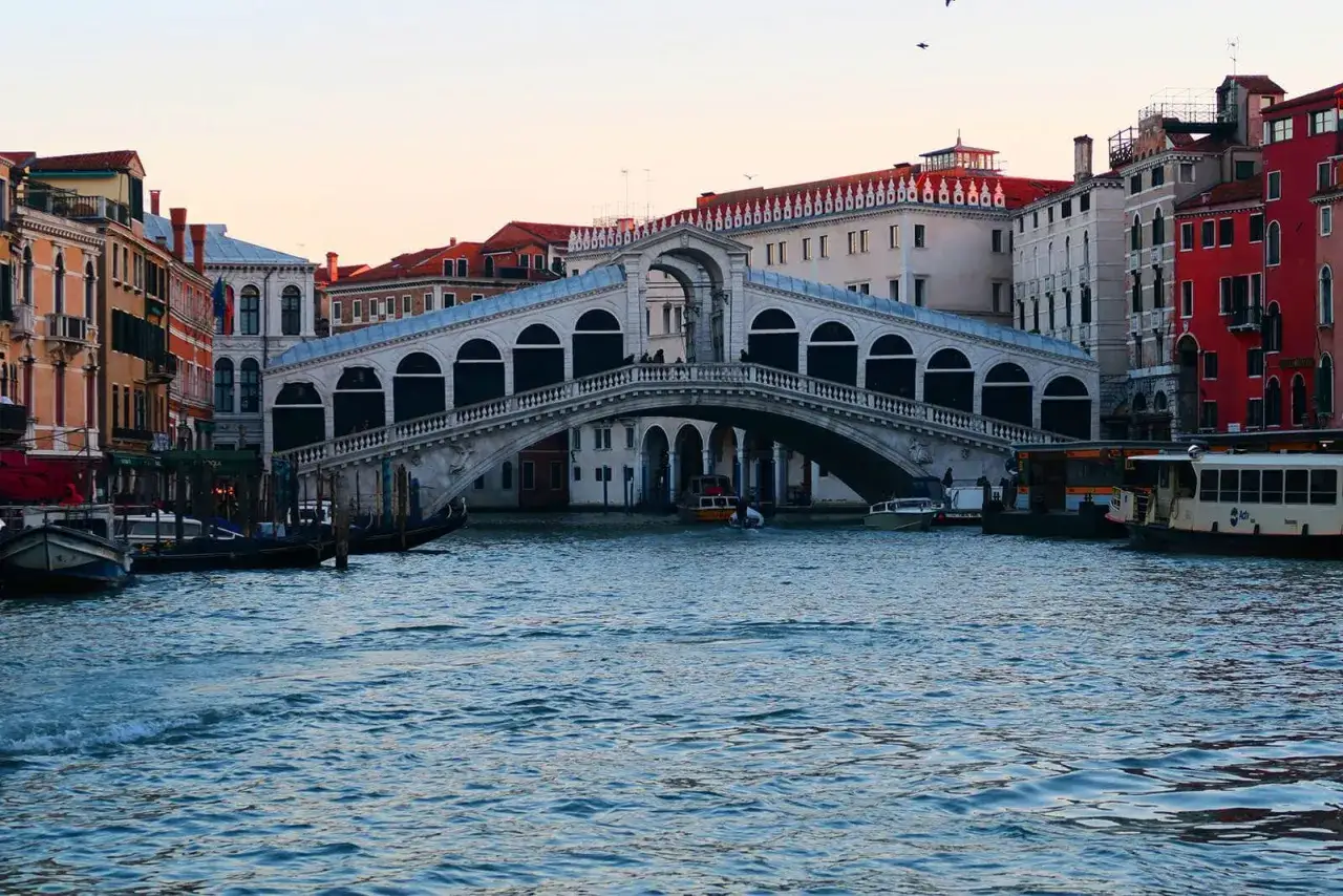 El puente de Rialto en Venecia, una vista ic&oacute;nica para tu plan de Venecia en 3 d&iacute;as. Barcos navegan por el canal.